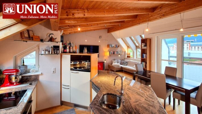 Gemütliche offene Wohnküche mit Holzdecke und großer Fensterfront, moderner Einrichtungsstil, Kochinsel mit Frühstücksbereich, komfortables Wohnzimmer, abwechslungsreiche Raumausstattung, perfekte Wohnatmosphäre, zentrale Lage, Alpenblick, stilvolles Zuhause.
