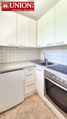 Helle, moderne Küchenzeile mit weißen Schränken, keramischem Kochfeld, Spüle und Mikrowelle, ideal für Immobilienangebote, Küche mit praktischem Stauraum und zeitgemäßem Design.