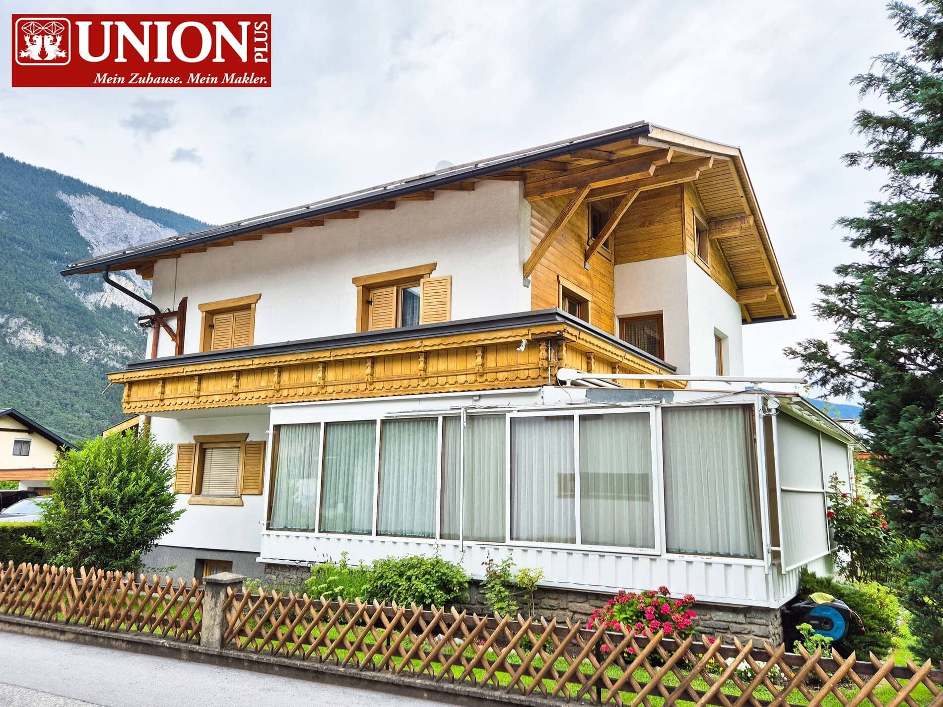 Gepflegtes Mehrfamilienhaus im alpinen Stil mit Holzverkleidungen und Balkon, umgeben von Grünflächen und Bergen, ideal für Familien und Immobilieninvestoren.