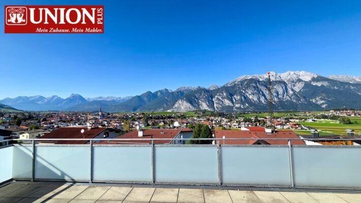 Hochwertiges Bild eines Bergpanoramas mit Blick auf eine österreichische Stadt und schneebedeckte Alpen im Hintergrund, aufgenommen von einem Balkon aus. Ideal für Inhalte zu Immobilien, Alpen, Berge, Stadtansichten und Natur in Österreich.