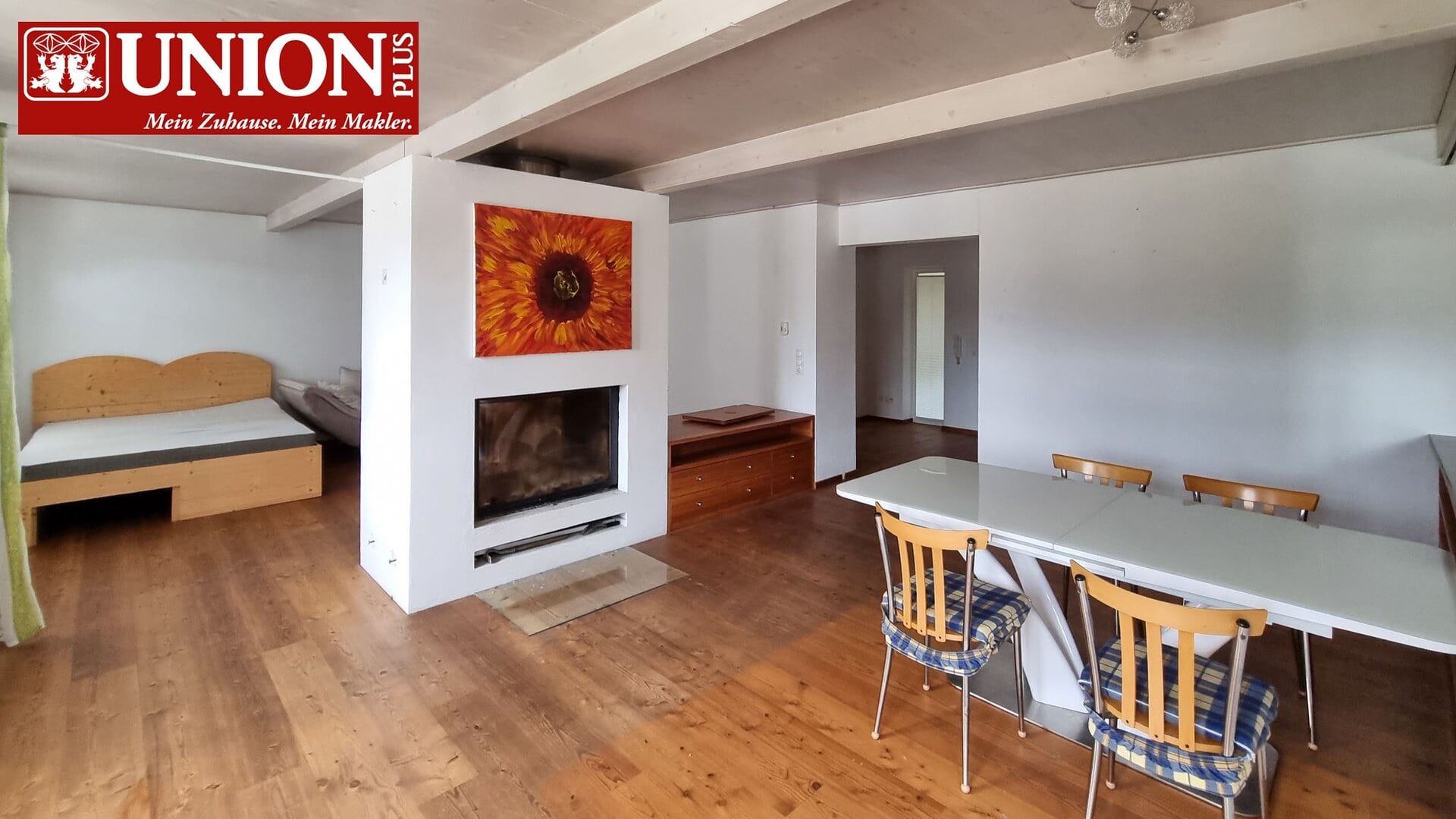 Helles Wohnzimmer mit Holzfußboden, einem Kamin, Essbereich mit weißen Tischen und Stühlen, Schlafzimmer im Hintergrund, gepflegtes und gemütliches Interieur, ideal für Familien oder Paare, moderner Wohnraum.