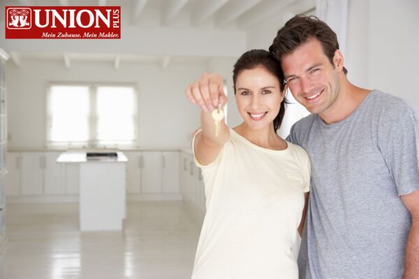 Glückliches Paar hält Schlüssel im modernen, hellen Zuhause, symbolisiert Sicherheit und neue Wohnträume. Perfekt für Immobilien- und Versicherungsthemen.