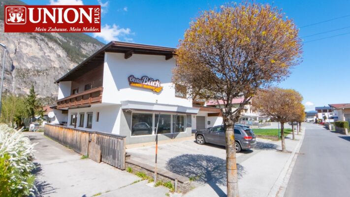 Charmantes Café mit Außenbereich und Parkplätzen in einer ruhigen Wohngegend, umgeben von Bäumen und Bergen, ideal für entspannte Treffen und Kaffee.